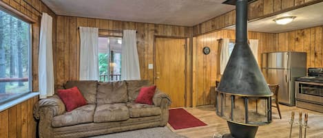 Un interior de cabaña acogedor con detalles de madera, un sofá, una chimenea y una zona de cocina.