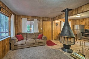L’intérieur chaleureux d’un chalet, avec un revêtement mural en bois, un canapé, une cheminée et un coin cuisine.