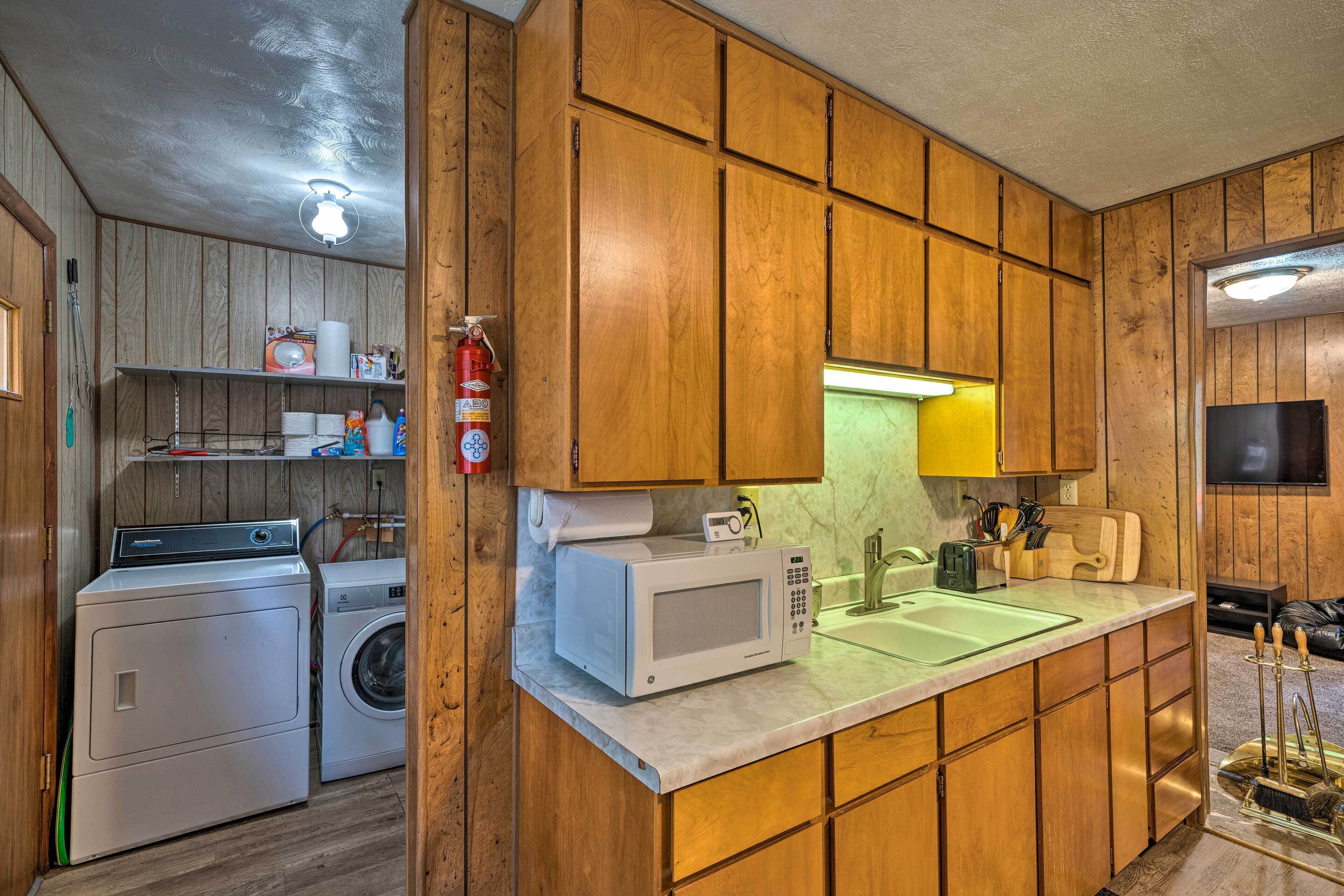 A compact kitchen with wooden cabinets, a microwave, a washing machine, and a sink.