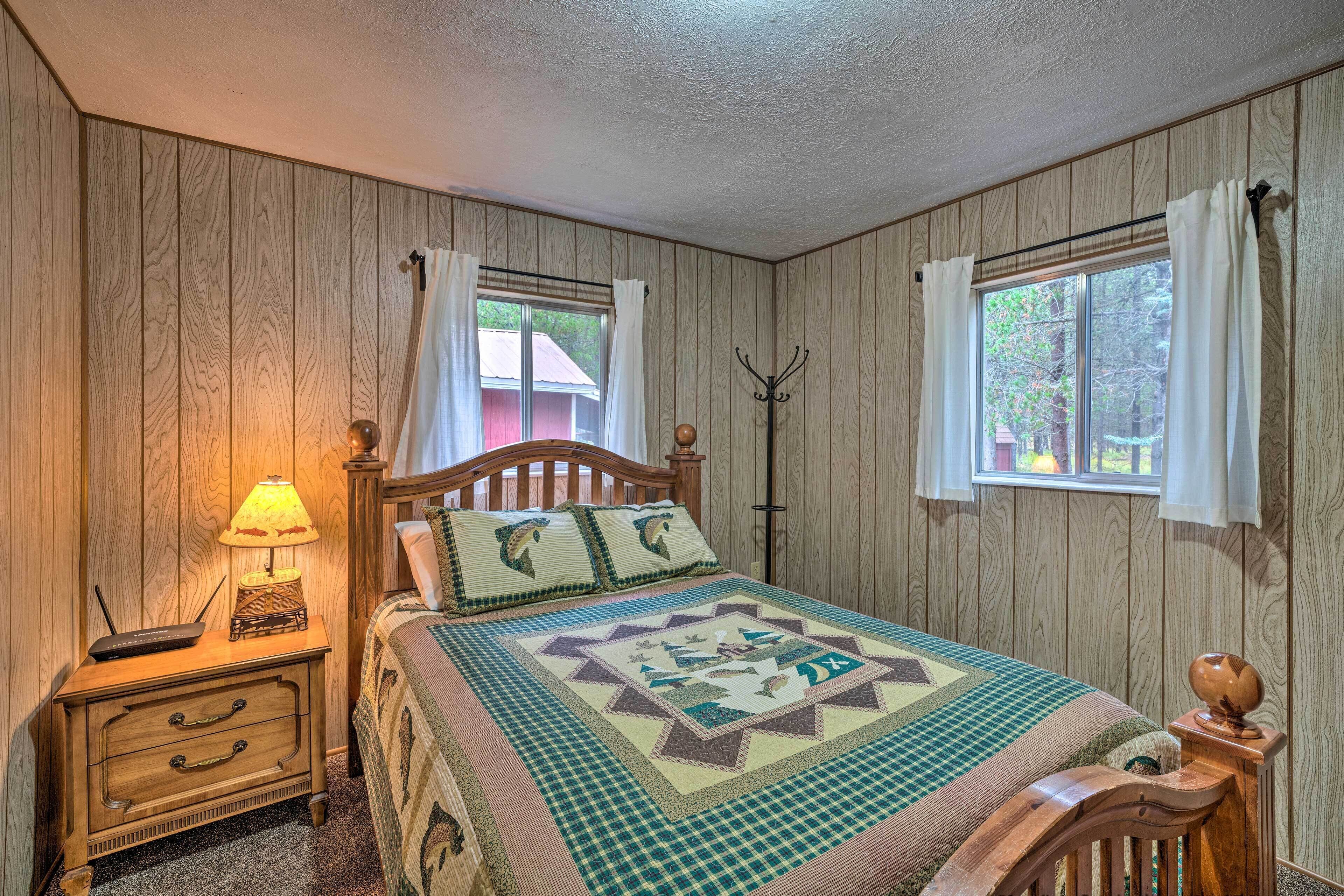 Een slaapkamer met een houten hoofdbord, een gewatteerde sprei, een nachtkastje met een lamp en een kapstok.