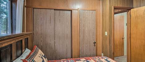 A bedroom with wooden panel walls, a bed with patterned bedding, and a window with curtains.