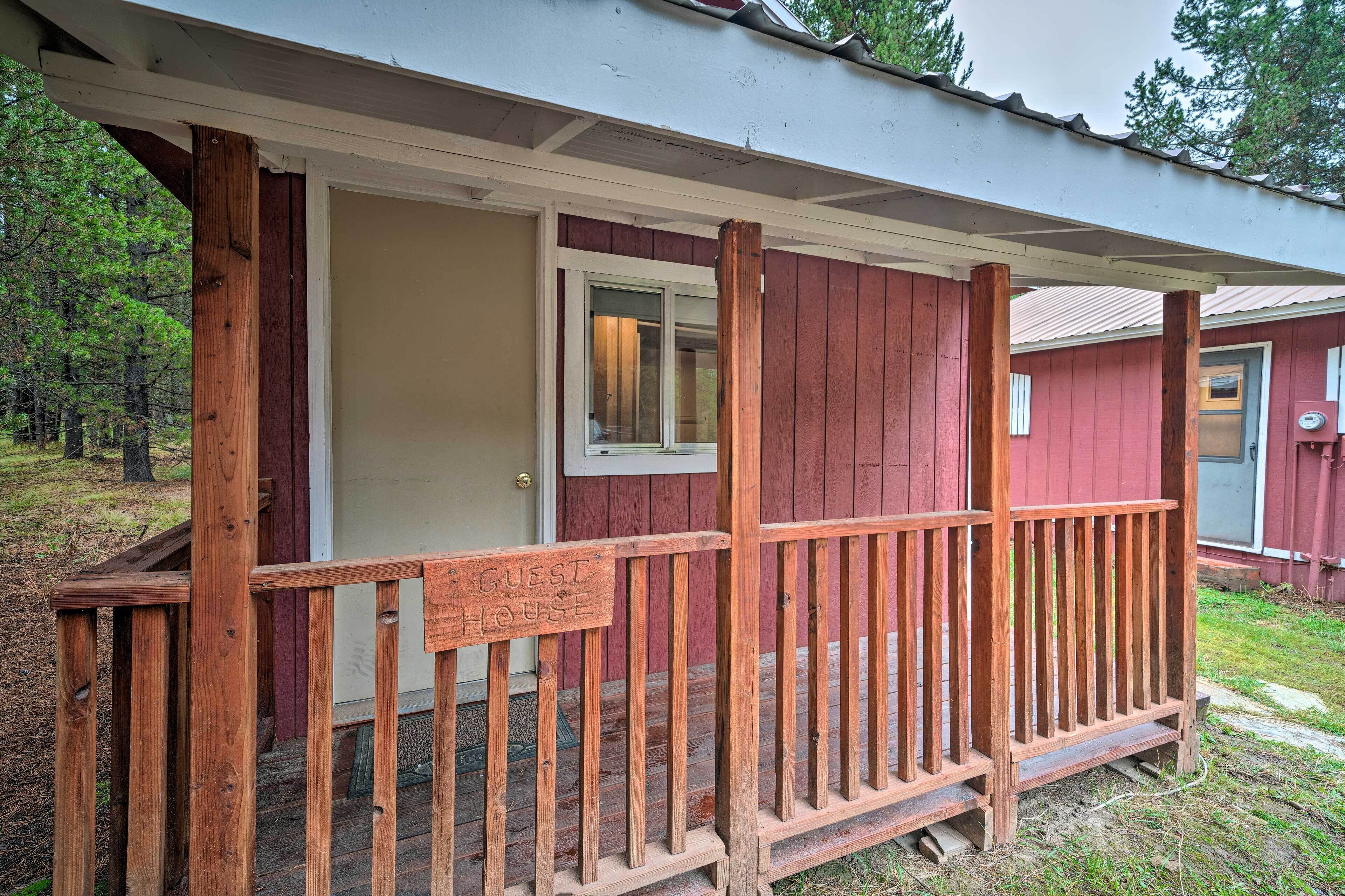 A wooden porch with a sign reading "GUEST HOUSE" and a door leading to a building with a red exterior.