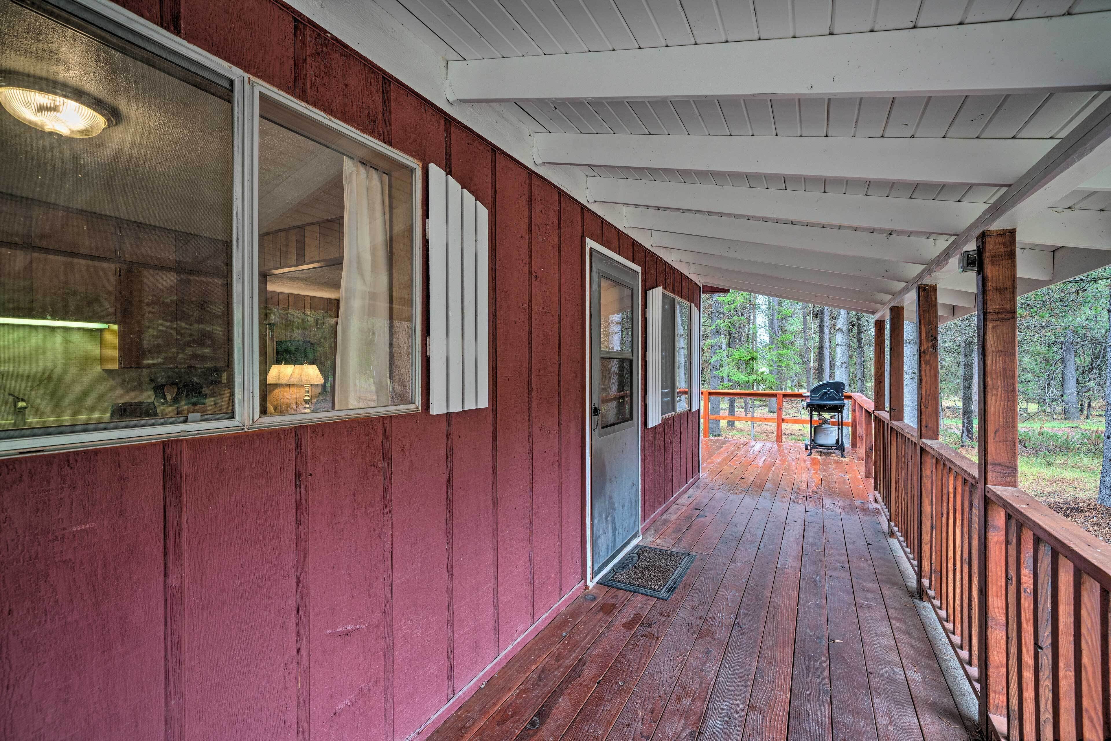 A covered wooden deck with a red exterior, a sliding glass door, and a view of the forest.