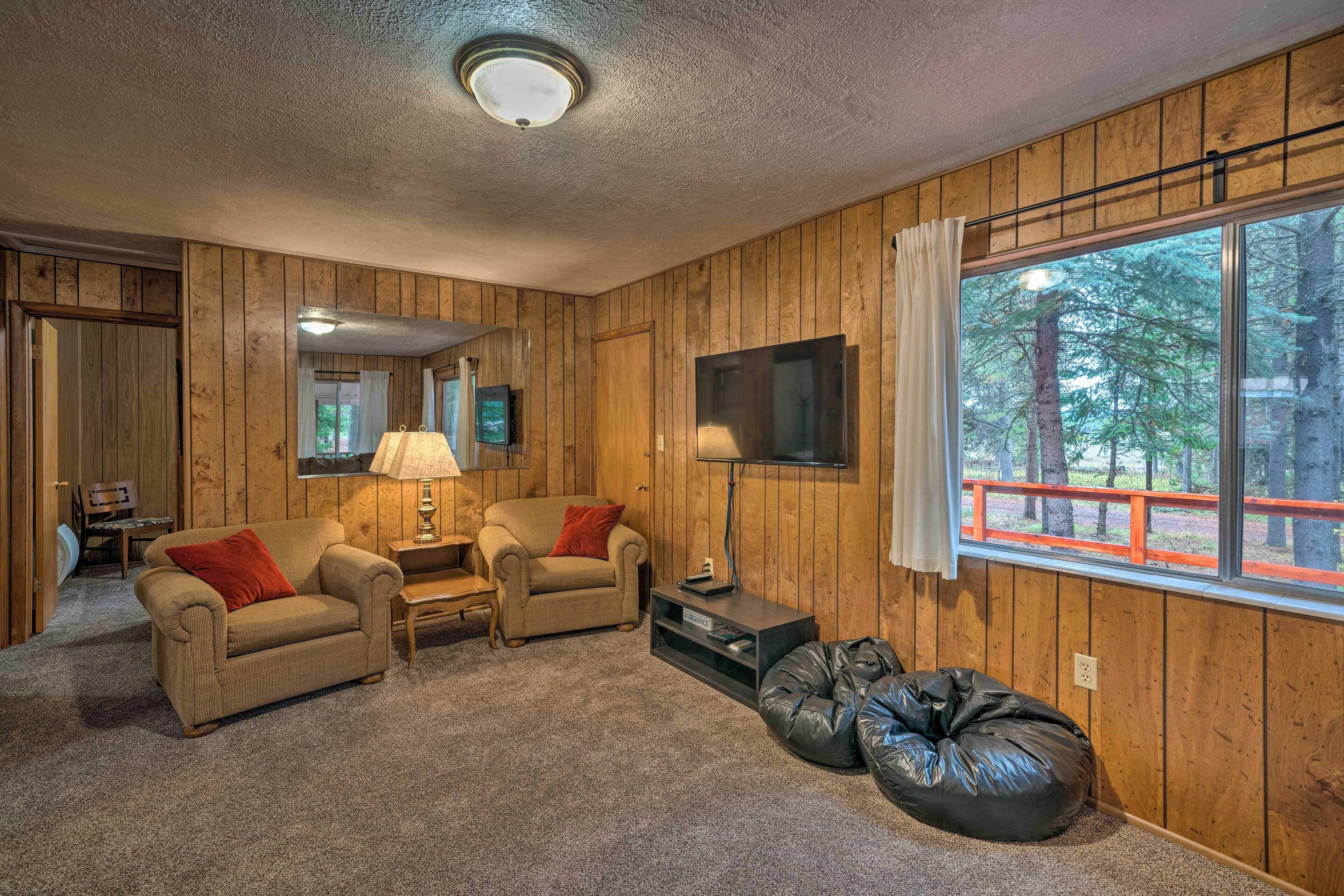 Una habitación acogedora con detalles de madera, un sofá, una silla, un televisor y una ventana con vistas a árboles.