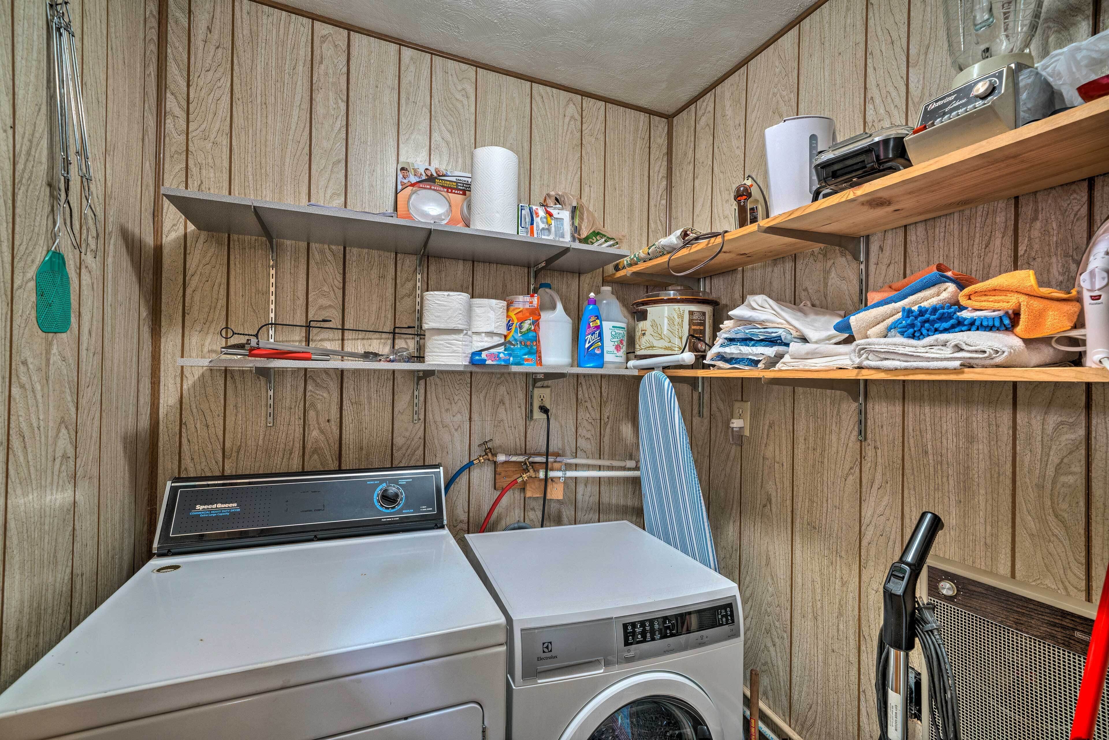 A laundry room with a front-loading washing machine, shelves with cleaning supplies, and a drying rack.