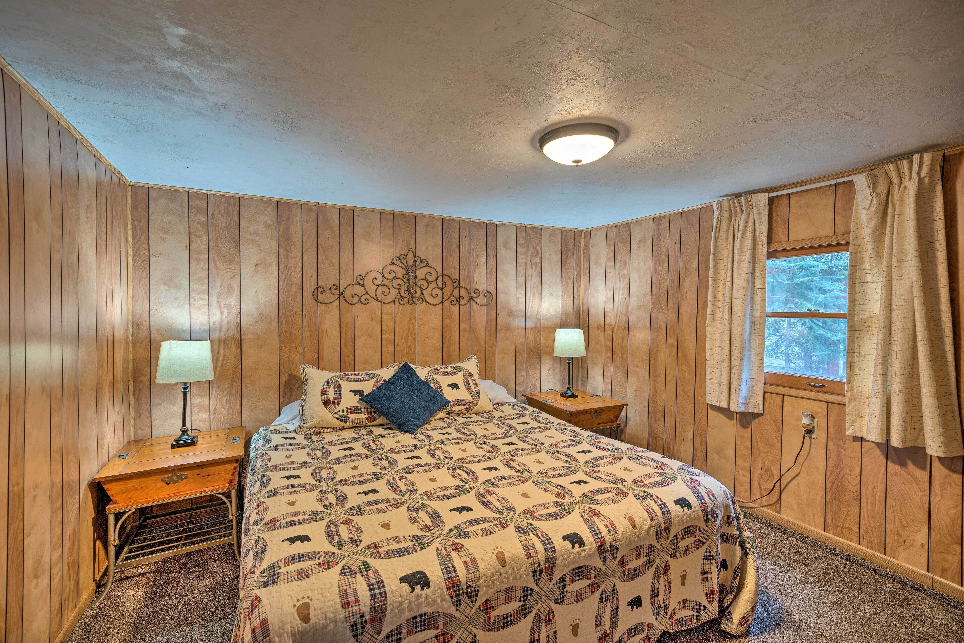 Un dormitorio con paneles de madera, una cama con colcha estampada, dos mesitas de noche con lámparas, una ventana con cortinas y una lámpara en el techo.
