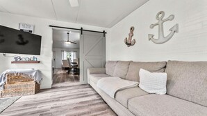 A modern living room with a beige sofa, a flat-screen TV, and nautical decor including anchors on the wall. - Beautiful house to relax and enjoy close to Camarillo outlets and beach (Camarillo)