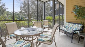 Eine überdachte Terrasse mit rundem Tisch, Stühlen und einer Sitzecke, mit Blick auf die umliegende Bepflanzung und Gebäude.