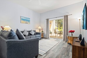 A modern living room with a grey sofa, two side tables with lamps, a large window with curtains, and a view of the outdoors. - Ground-Floor Bahama Bay Condo • 2BR/2BA • Pools, Hot Tubs & Patio (Davenport)