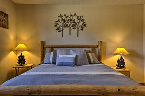 A neatly made bed with a wooden headboard, two bedside tables with lamps, and a wall decoration above the bed. - Eat, Sleep, Ski! Rustic Mtn Condo: WiFi,TV, HotTub (Fraser)