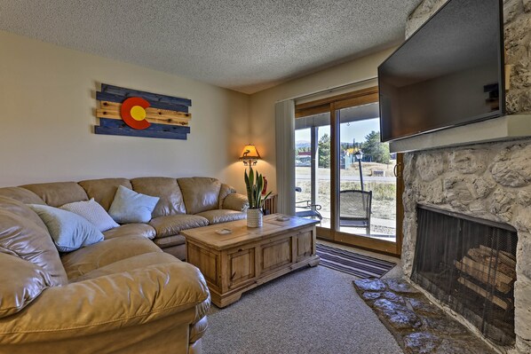 A living room with a stone fireplace, a leather sofa, and a large window. - Eat, Sleep, Ski! Rustic Mtn Condo: WiFi,TV, HotTub (Fraser)