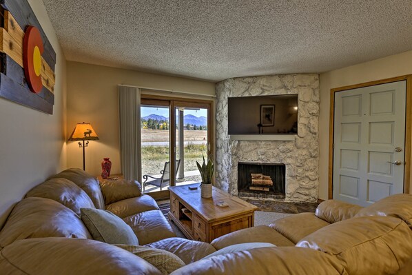 A cozy living room with a stone fireplace, leather sofas, and a view of the outdoors. - Eat, Sleep, Ski! Rustic Mtn Condo: WiFi,TV, HotTub (Fraser)