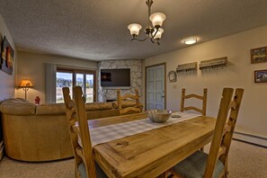 A cozy living room with a large sofa, wooden dining table, and a TV mounted on the wall. - Eat, Sleep, Ski! Rustic Mtn Condo: WiFi,TV, HotTub (Fraser)