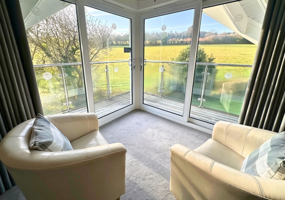 A corner room with two leather sofas, a glass door leading to a balcony with a view of a field.