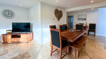 A modern dining area with a wooden table and chairs, a clock on the wall, and a television on a wooden stand.