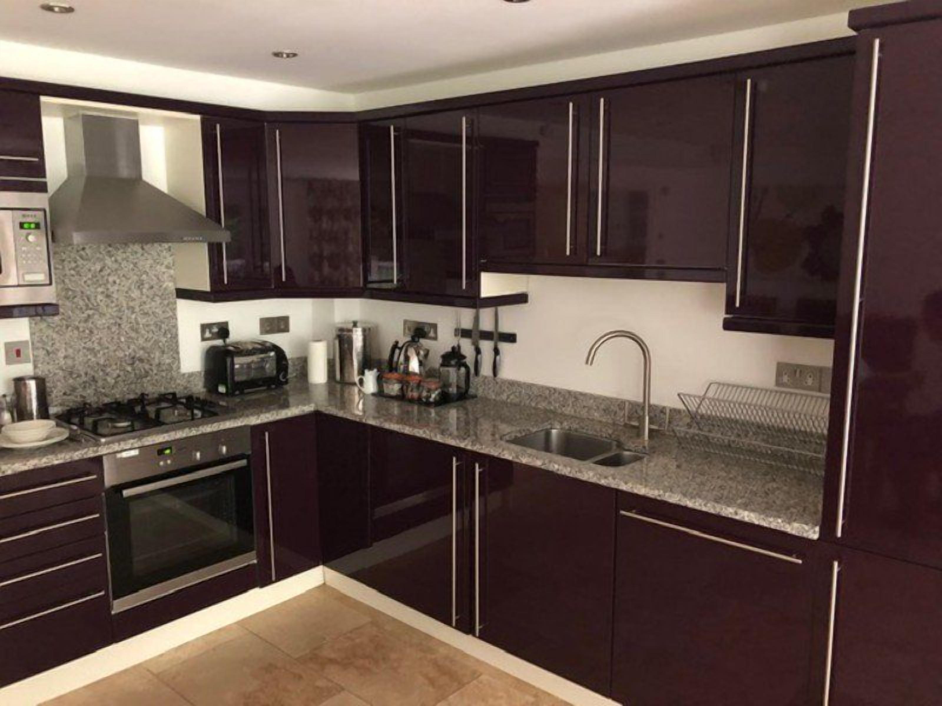 A modern kitchen with dark cabinets, a granite countertop, a gas stove, a built-in oven, a stainless steel sink, and a range hood.