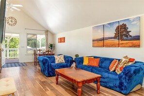 A living room with a blue sofa, wooden coffee table, and a large landscape painting. - Classic Red Barn Loft w/Views in the Heart of Paso Wine Country & Pet Friendly! (Templeton)