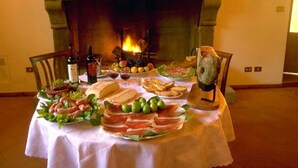 A dining table set with various foods and drinks, a fireplace in the background, and a painting on the wall.