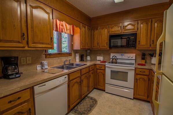 A kitchen with wooden cabinets, a dishwasher, an oven, a microwave, and a window with blinds.