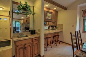 A kitchen with wooden cabinets, a sink, and bar stools. - Charming Condo on Sugar w/ Access to Clubhouse (Sugar Mountain)