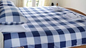 A neatly made bed with a checkered blue and white bedspread, a pillow, and folded towels on the side. - Meadowside Apartment (Fowey)