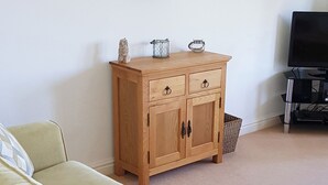 A wooden cabinet with drawers and a shelf, a wicker basket, a small owl figurine, and a television on a stand. - Meadowside Apartment (Fowey)