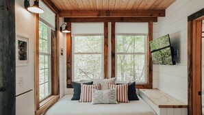 Un dormitorio acogedor con cama, ventanas amplias, vigas de madera y un televisor en la pared.