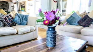 Ett vardagsrum med två soffor, ett träbord och en vas med blommor, samt en klocka på väggen.