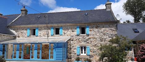A stone house with blue shutters, a balcony, and a gravel driveway.