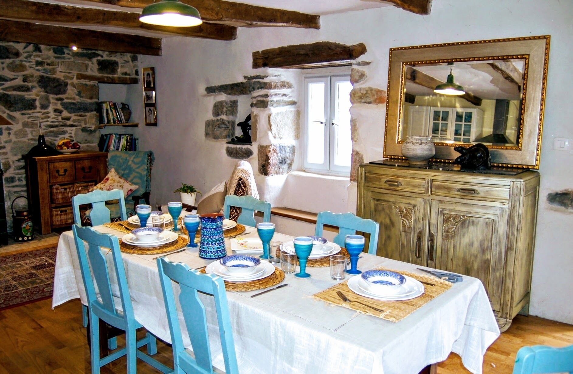 Ein Esszimmer mit Steinwand, Holzbalken, einem großen Spiegel und einem Tisch, gedeckt für sechs Personen, mit blau-weißen Tellern und Gläsern.