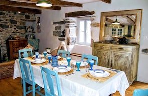 A dining room with a stone wall, wooden beams, a large mirror, and a table set for six with blue and white plates and glasses.