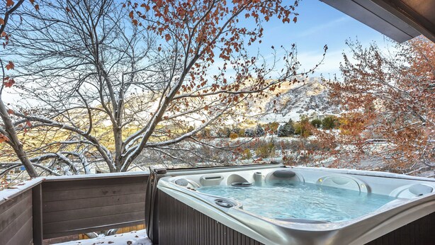 Un jacuzzi con terraza de madera y vistas a un paisaje nevado y árboles.