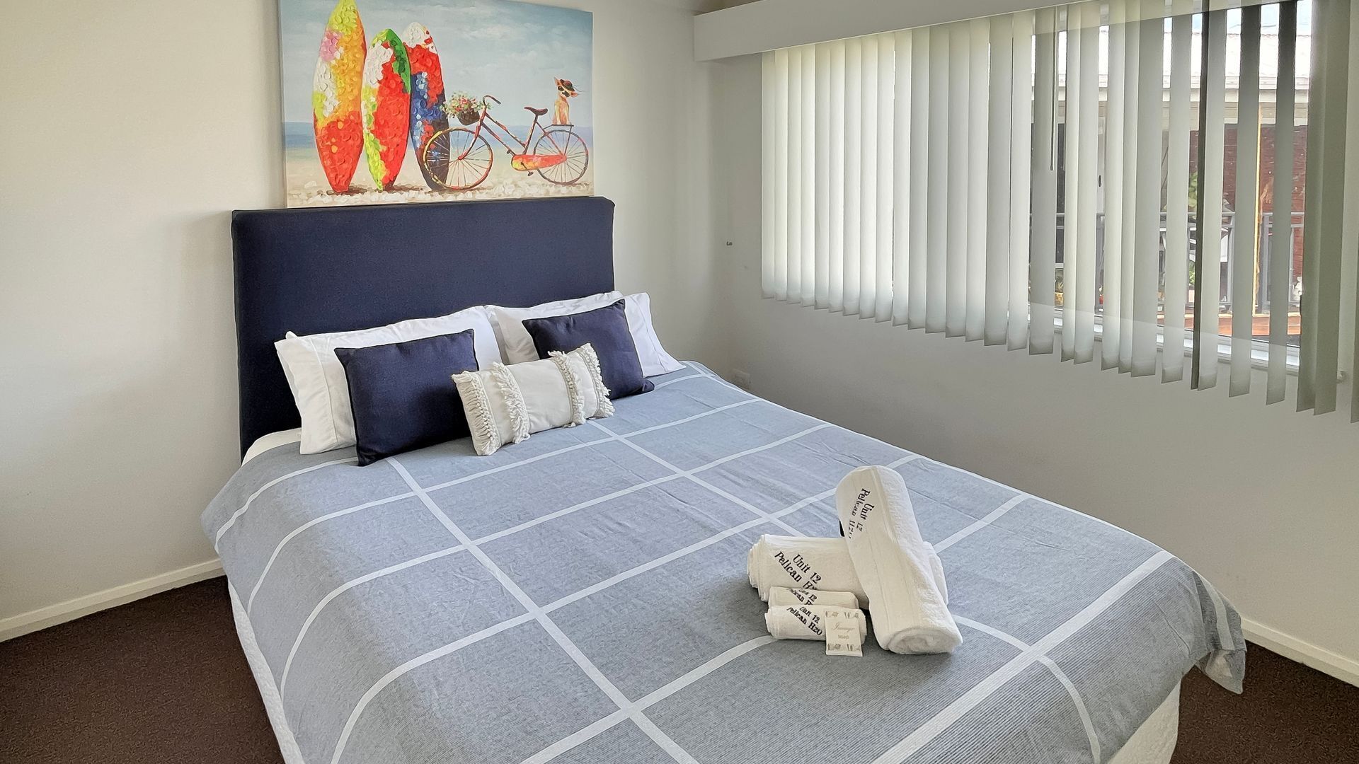 Un lit bien fait, recouvert d’une couverture à carreaux bleus et blancs, avec deux oreillers et une serviette pliée posée sur le lit.
