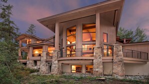 A modern multi-story house with large windows, stone pillars, and a balcony.
