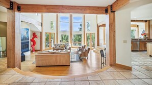 A spacious living area with a large sofa, a fireplace, and a view of the outdoors through large windows.