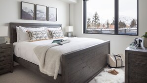 A bedroom with a large window, a wooden bed, a nightstand, and a dresser.