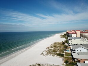 Une plage avec une jetée, une étendue de sable blanc et une rangée de bâtiments dotés de balcons donnant sur la plage.