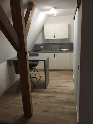 Eine kompakte Küche mit Essbereich, inklusive eines Holzbalkens an der Decke, einem kleinen Tisch mit Stuhl und weißen Schränken.