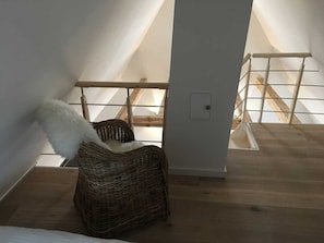 A loft bedroom with a high ceiling, a wooden floor, a wicker chair, and a white wall. - Apartment B OG (on 2 floors) - Christmann's Cottage Apartment An on the ground floor and (Weisenheim am Berg)