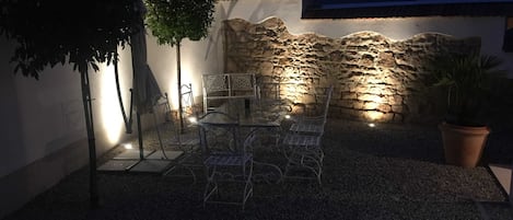 Un patio al aire libre con un muro de piedra, sillas de metal y una mesa.