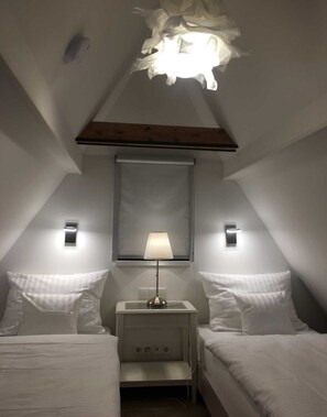 A bedroom with a sloped ceiling, two bedside tables with lamps, a bed with white bedding, and a large mirror above the bed. - Apartment B OG (on 2 floors) - Christmann's Cottage Apartment An on the ground floor and (Weisenheim am Berg)