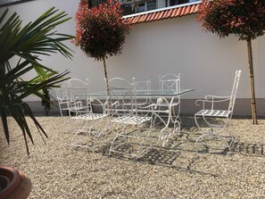 A white metal outdoor table and chairs set on gravel, with two small trees and a potted plant nearby. - Apartment B OG (on 2 floors) - Christmann's Cottage Apartment An on the ground floor and (Weisenheim am Berg)