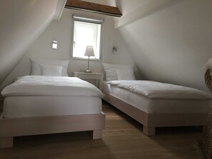 A bedroom with two beds, a small table, a lamp, and a window. - Apartment B OG (on 2 floors) - Christmann's Cottage Apartment An on the ground floor and (Weisenheim am Berg)