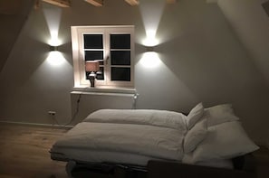 A bedroom with a bed, a window with two wall-mounted lights, and a radiator. - Apartment B OG (on 2 floors) - Christmann's Cottage Apartment An on the ground floor and (Weisenheim am Berg)