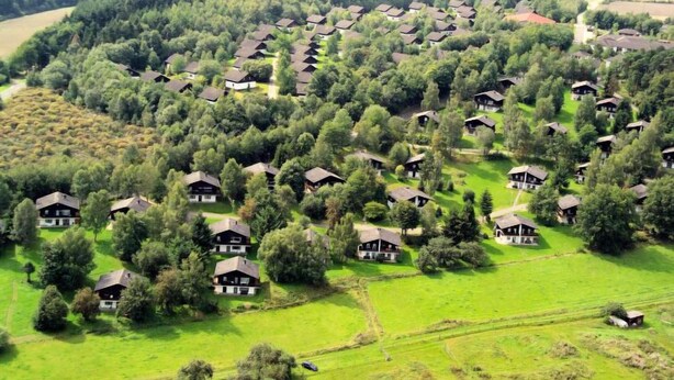 Vista aérea de um bairro residencial com várias casas, rodeado por campos verdes e árvores.