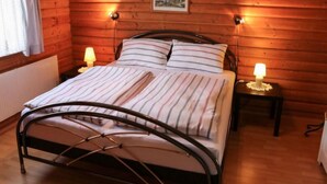 Quarto com painéis de madeira, uma cama, duas luminárias de cabeceira e um quadro na parede.