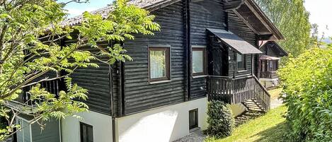 A two-story log cabin with a balcony and a small attached shed.
