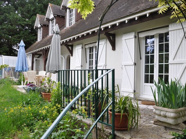 A white building with a porch, potted plants, and outdoor furniture.