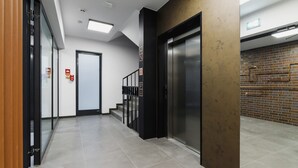 Ein moderner Aufzugsbereich mit einem metallenen Aufzug, einem Brandmelder und einer Treppe, die zu einer anderen Etage führt.