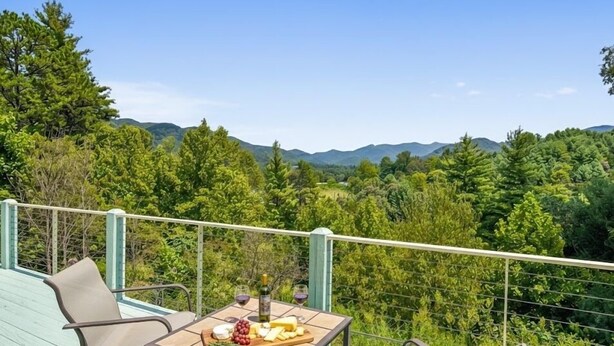 Un balcón con una mesa dispuesta para una comida, con vista a un paisaje boscoso.